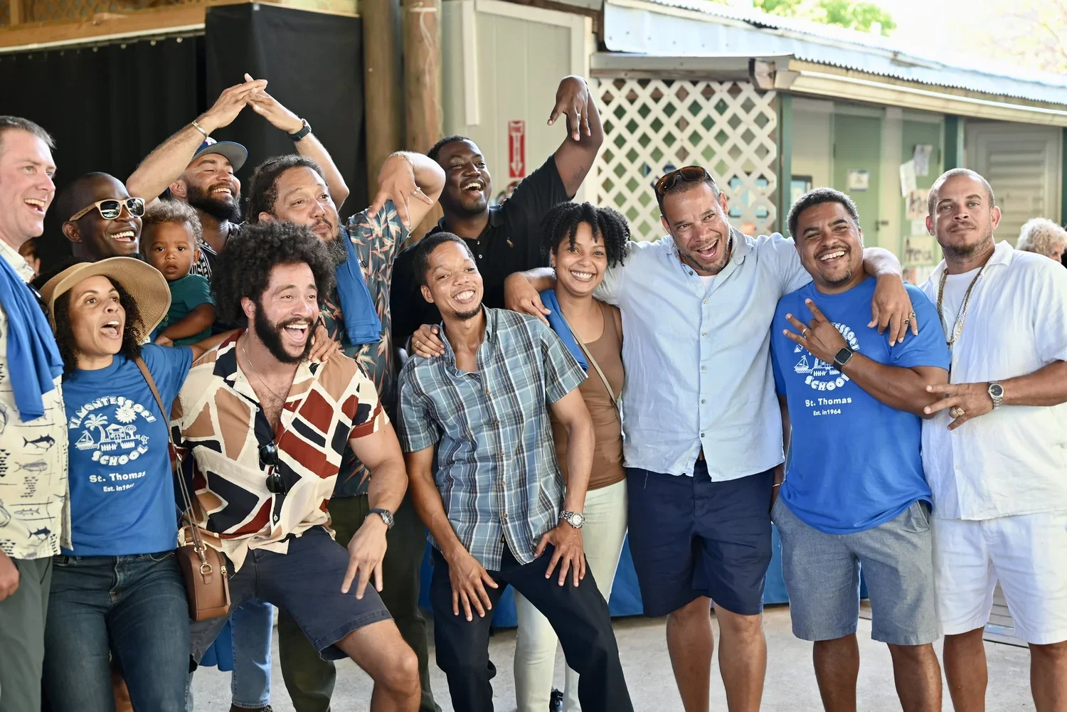 Group of diverse people smiling and celebrating together outdoors, some with their arms around each other, at a social gathering or event.