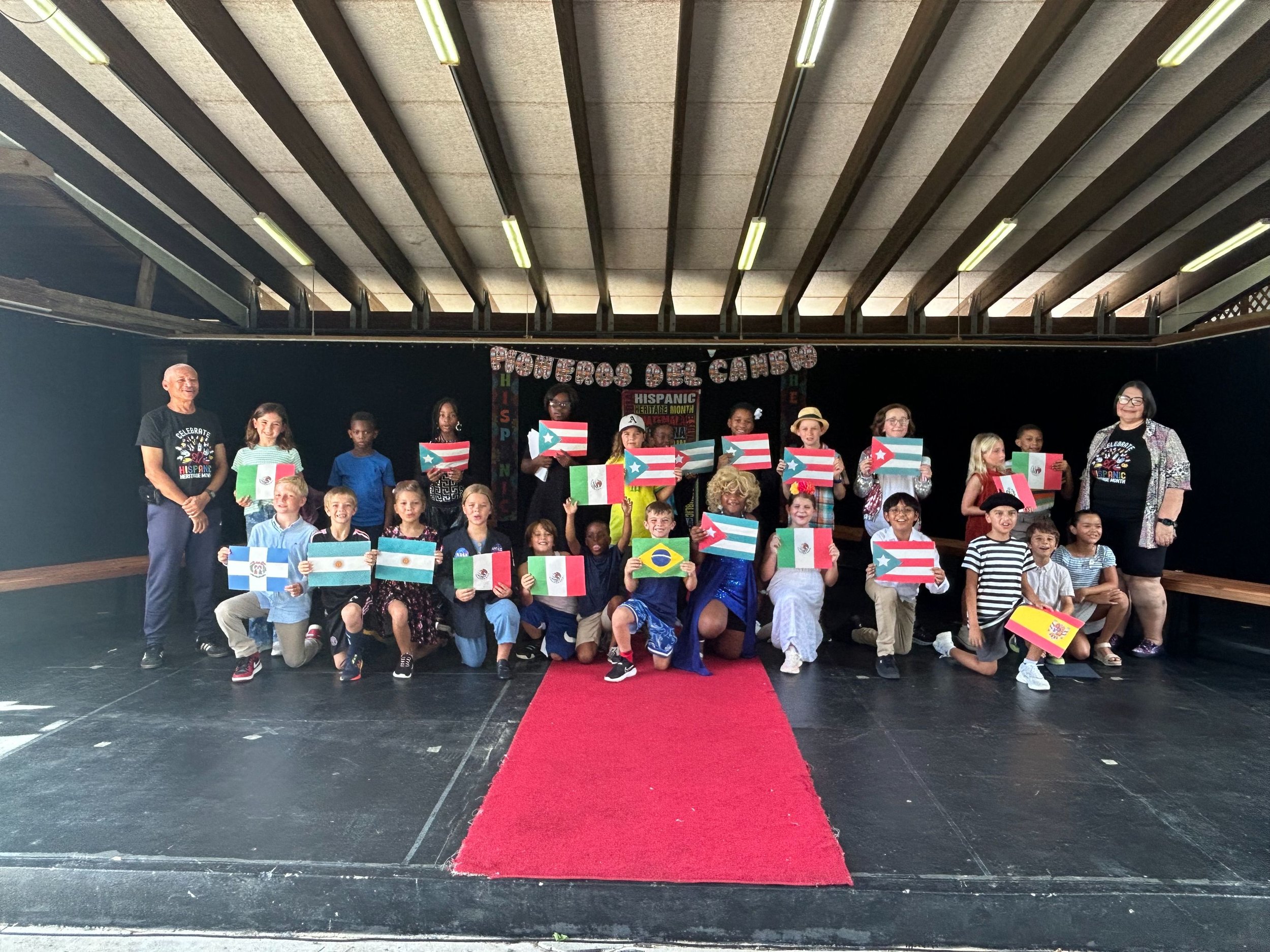 Group of children and two adults on stage holding Puerto Rican flags during Hispanic Heritage Month celebration.