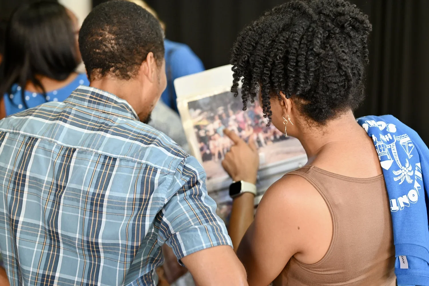 People looking at a photo album or scrapbook together at an indoor event, with two women and one man visible from behind.
