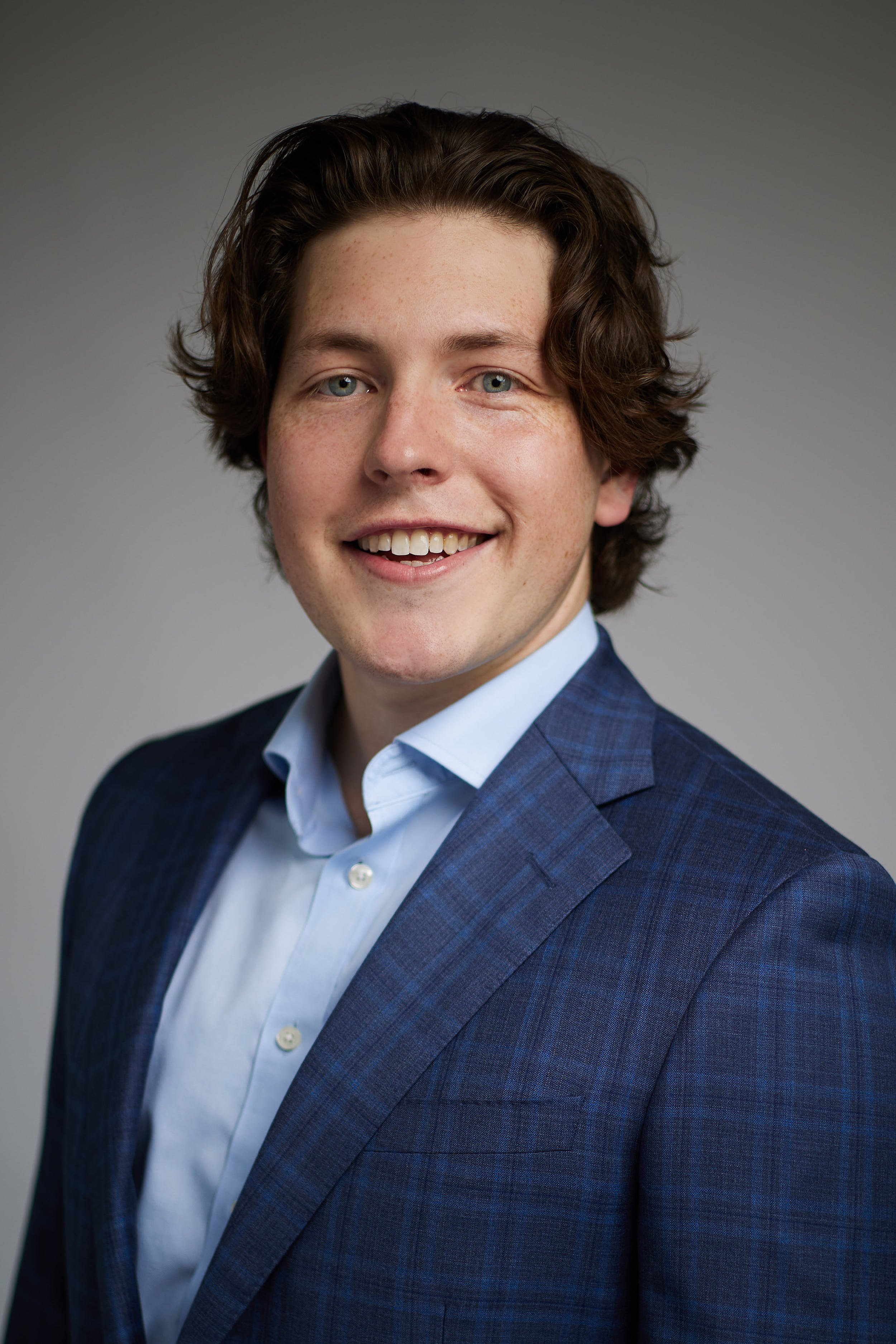 Headshot of young man smiling wearing a blue suit.
