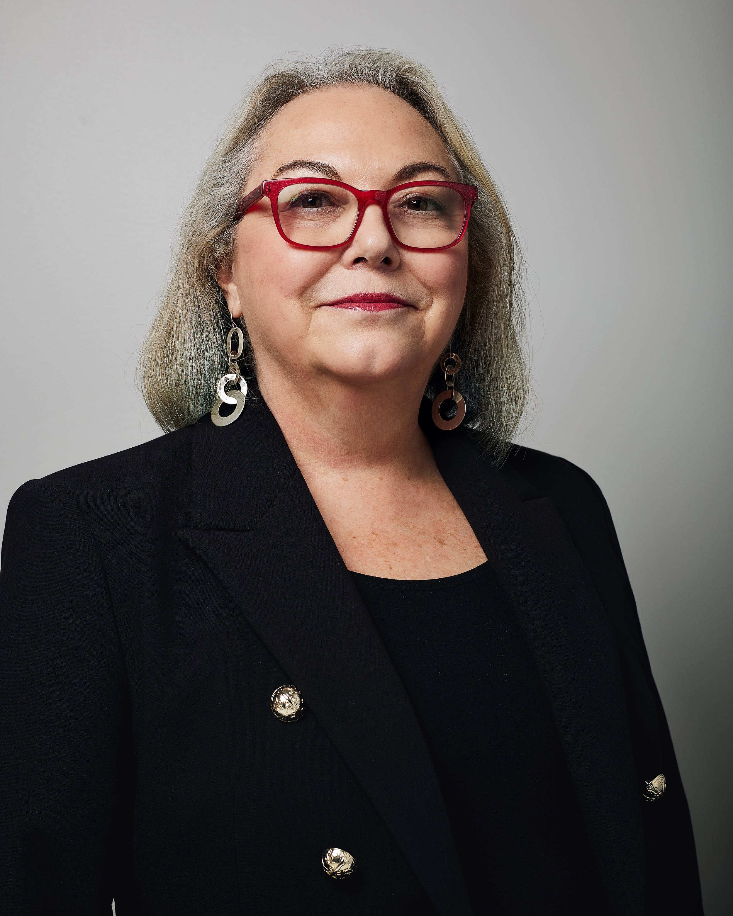 Headshot of woman in red glasses on gray background.