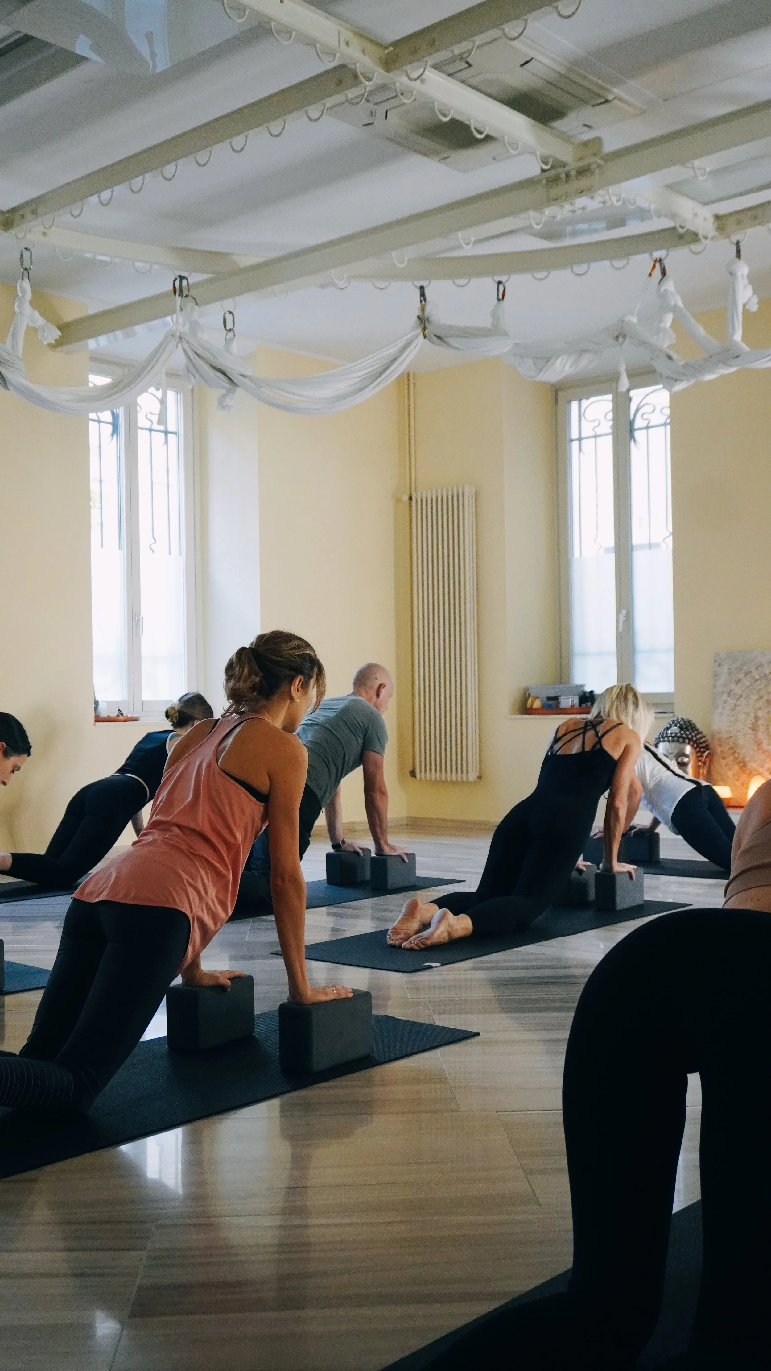 Persone che fanno yoga in una sala illuminata con grandi finestre e decorazioni sospese dal soffitto.