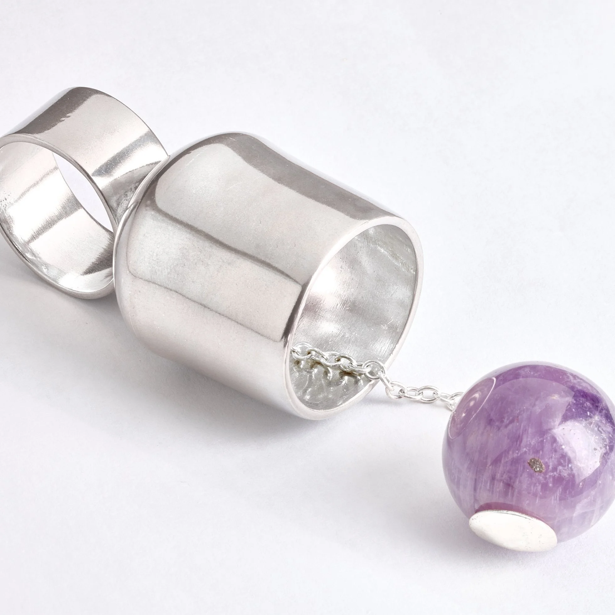 Silver cup and ball ring with an amethyst bead as the ball attached by a chain on a white background.