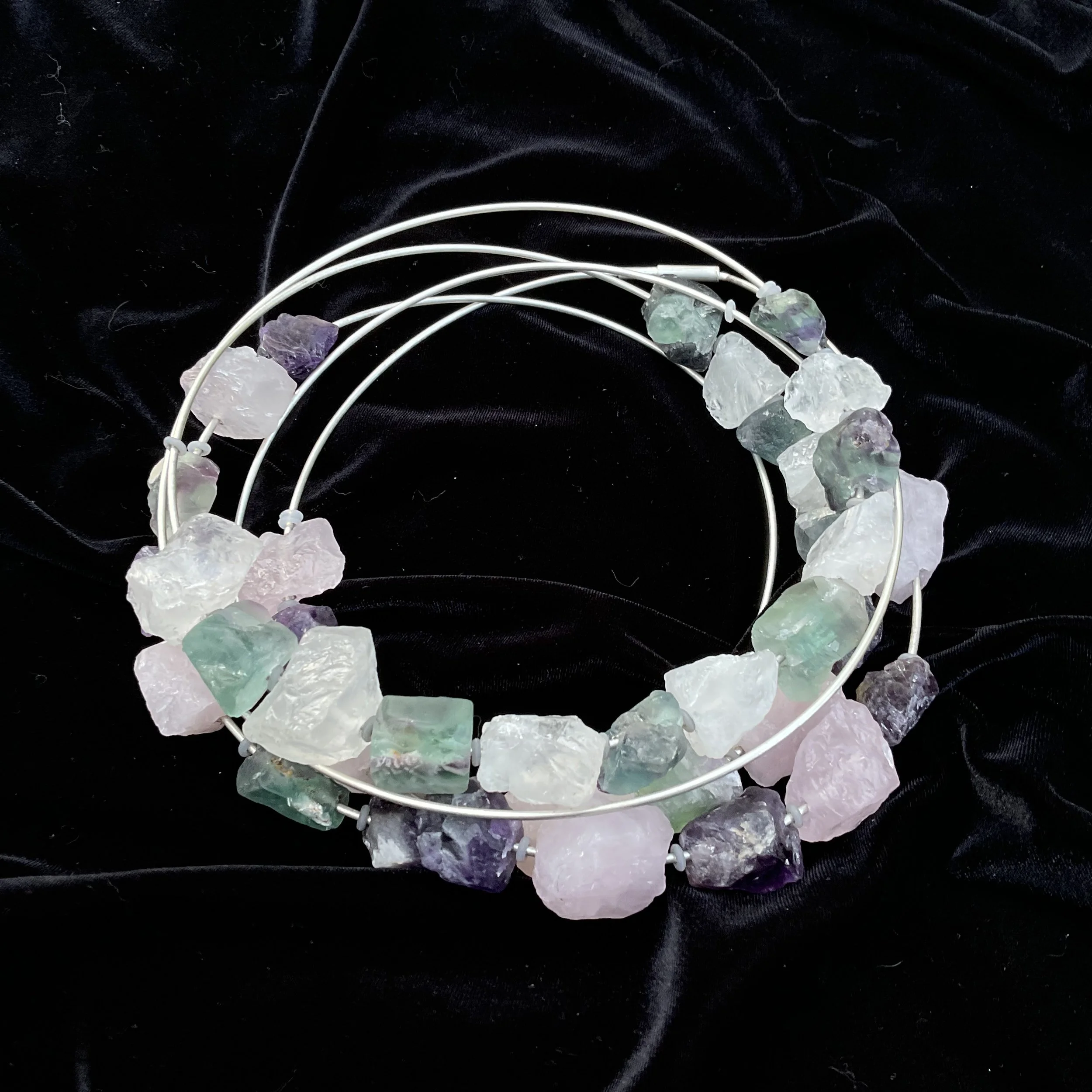 A neckpiece in silver with colorful rough gemstone beads resting on black fabric.