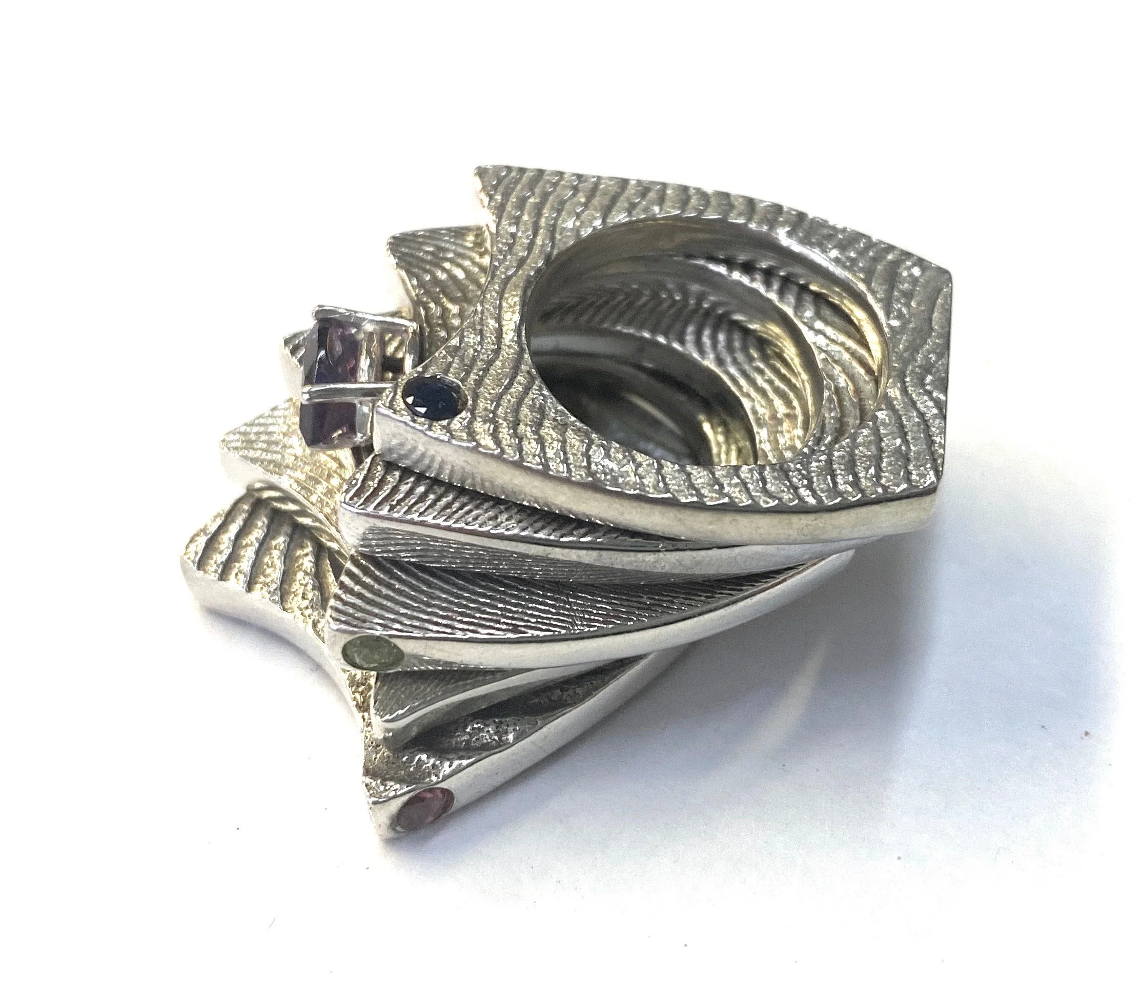 A cuttlebone cast stacking ring designed in the shape of a feather with small gemstones set in it.