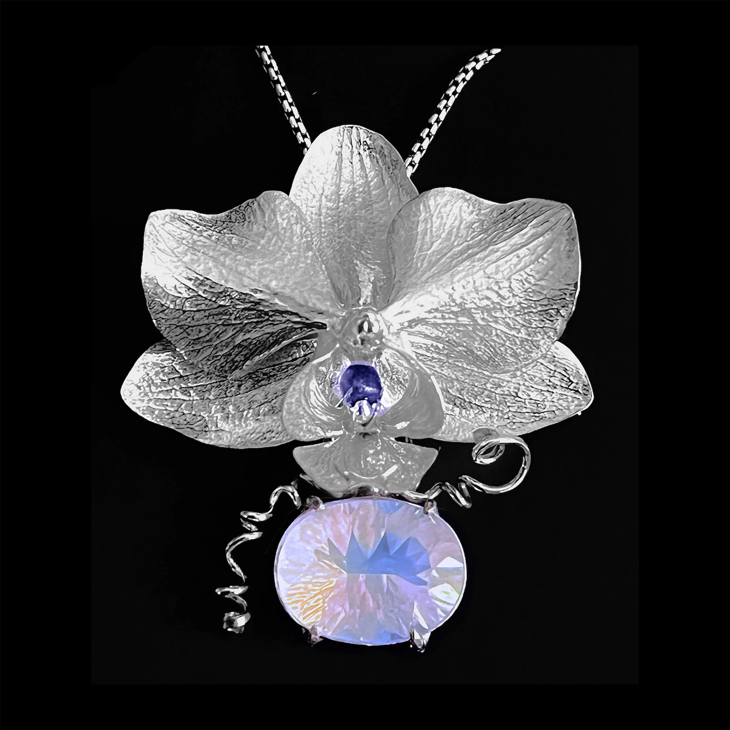 Silver orchid necklace with a cast in place sapphire and large, blue moon quartz gemstone pendant on a silver chain against a black background.