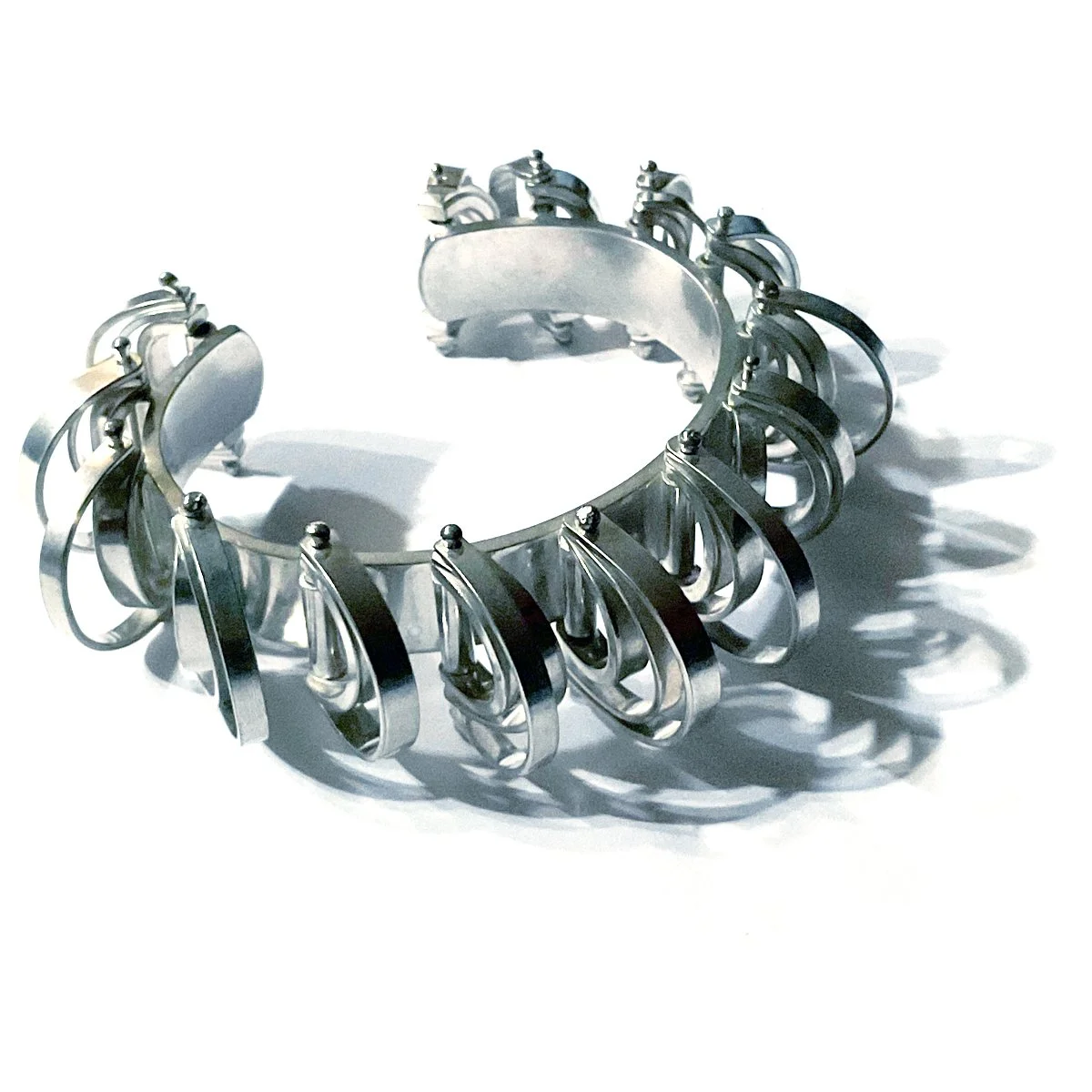 Silver kinetic cuff bracelet casting shadows on a white surface.