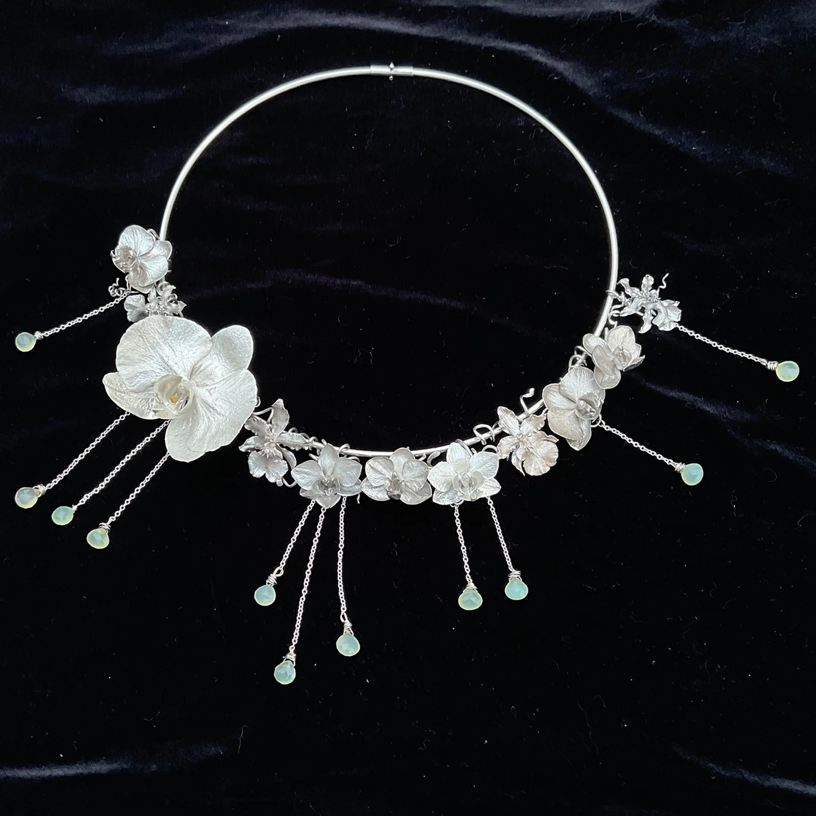 Silver orchid necklace with hanging chalcedony bead accents on black fabric background.