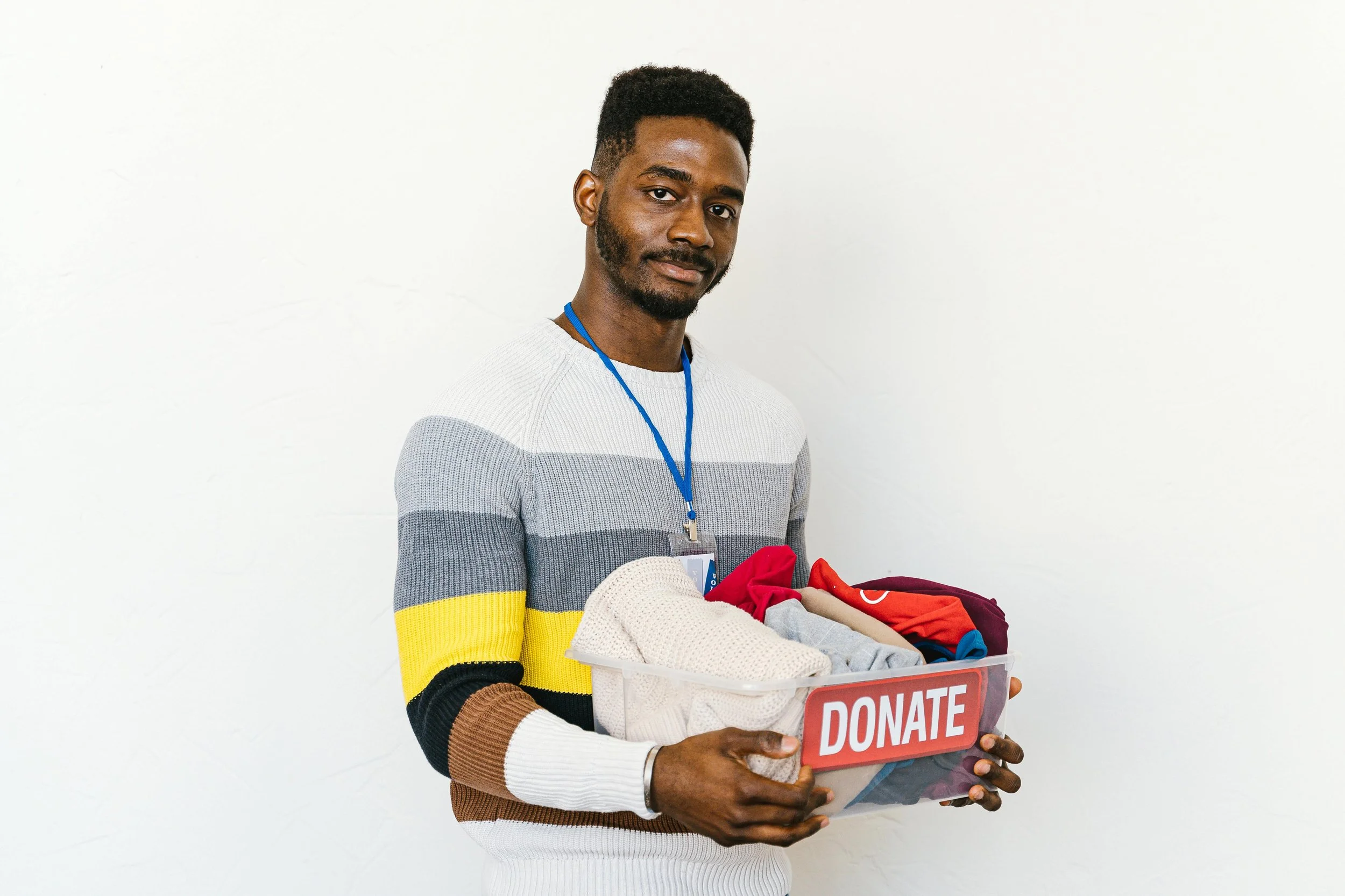Man holding a donation box filled with clothing, standing against a white background.