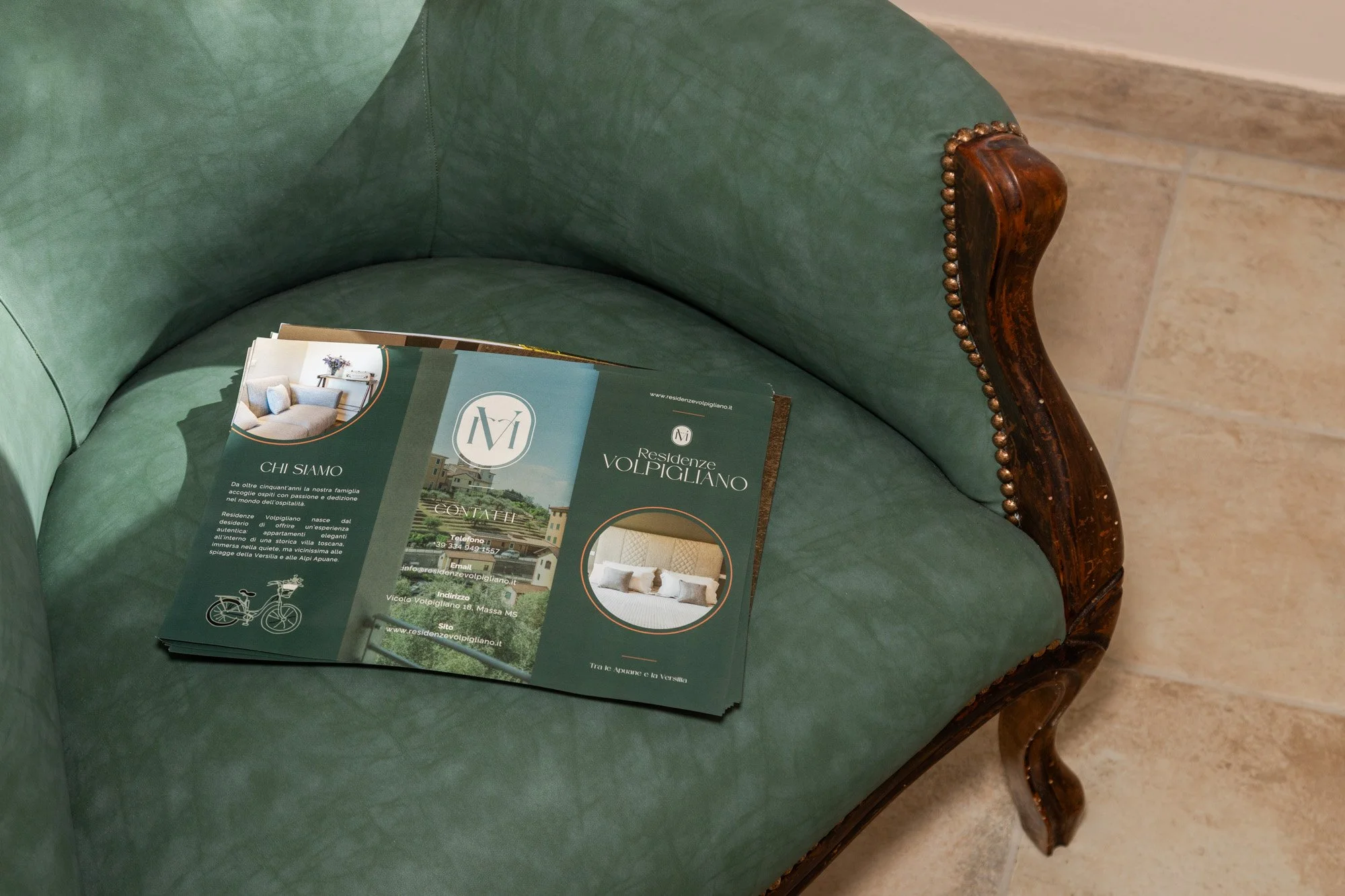 Firma pubblicitaria per le Residenze Volpigliano appoggiata su un divano di colore verde con dettagli in legno.