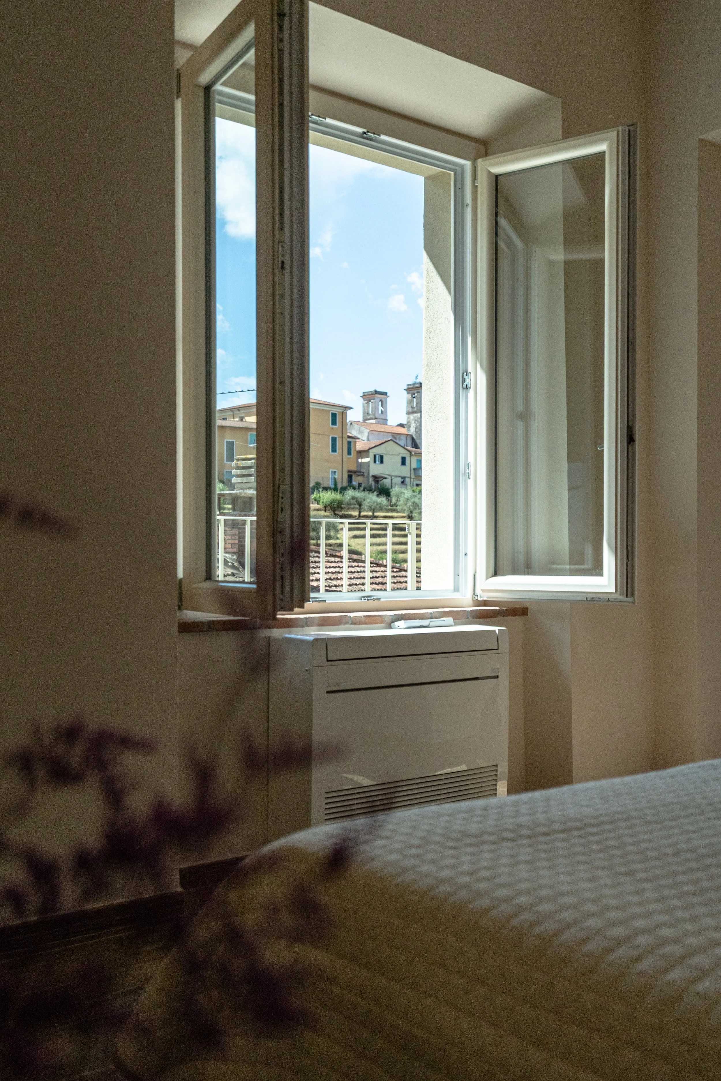 Finestra aperta in una stanza con vista su case, aria fresca entra nell'ambiente. - Residenze Volpigiano