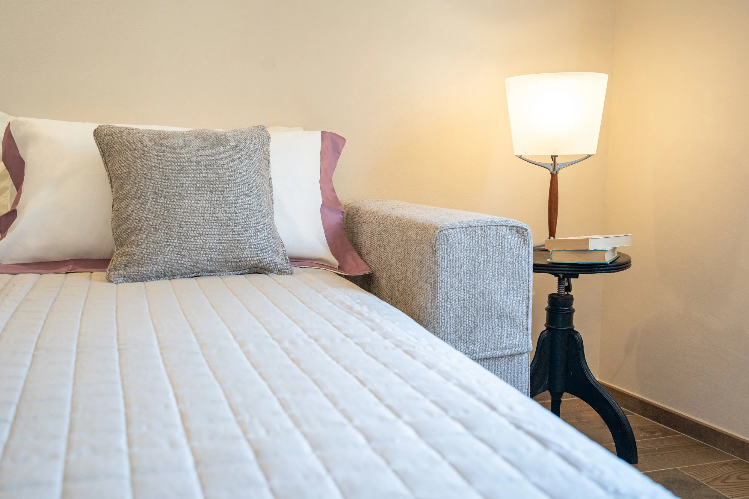 Letto con cuscino grigio, letto con coperte bianche, lampada da tavolo con libri su un lato del letto in una camera da letto - Residenze Volpigiano