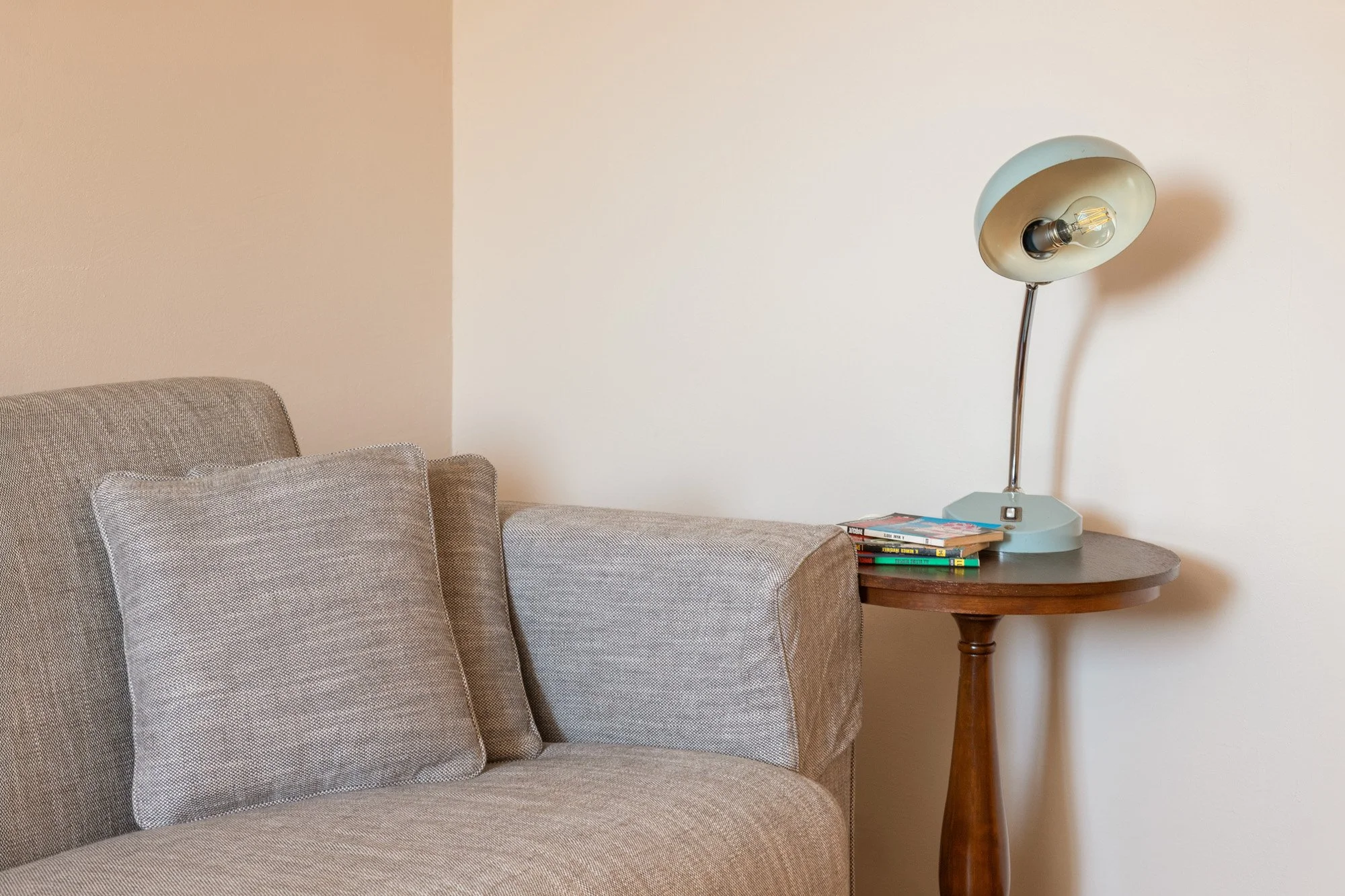 Soggiorno con divano beige, cuscini e lampada da tavolo su un tavolo di legno vicino al muro