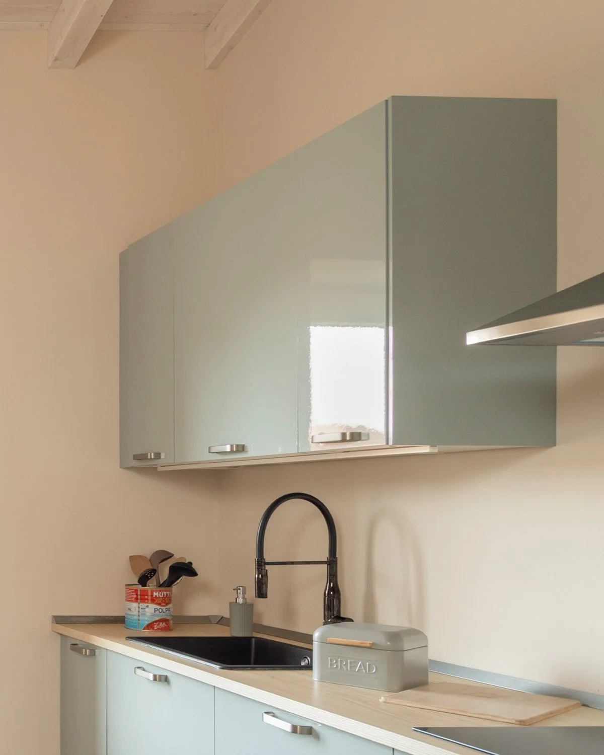 Una cucina moderna con armadietti azzurri, lavabo nero, rubinetto nero, contenitore per il pane, piatto in legno, bottiglia di sapone e utensili da cucina.