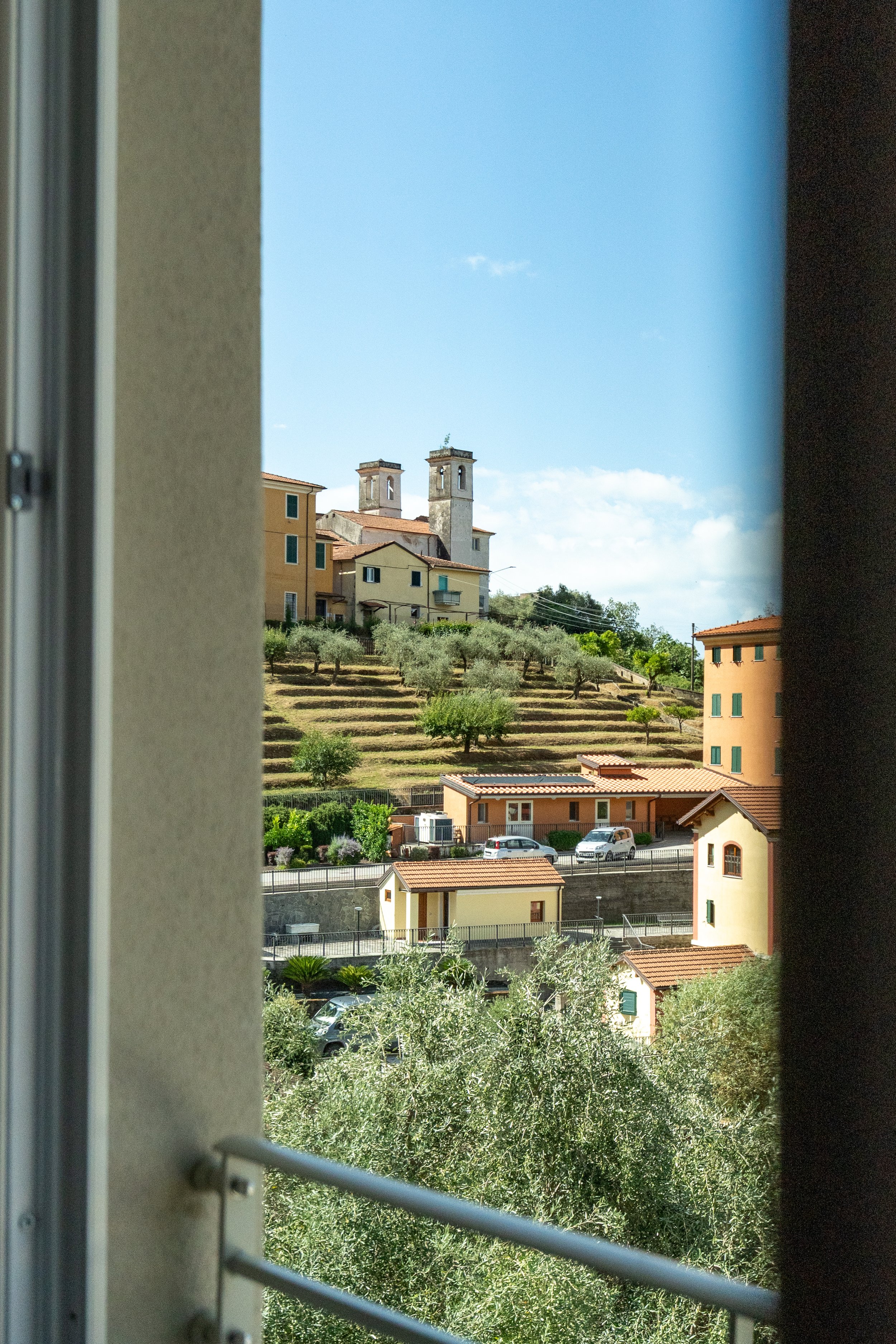 Vista di un paesaggio collinare con case colorate e alberi, vista attraverso una finestra - Residenze Volpigiano