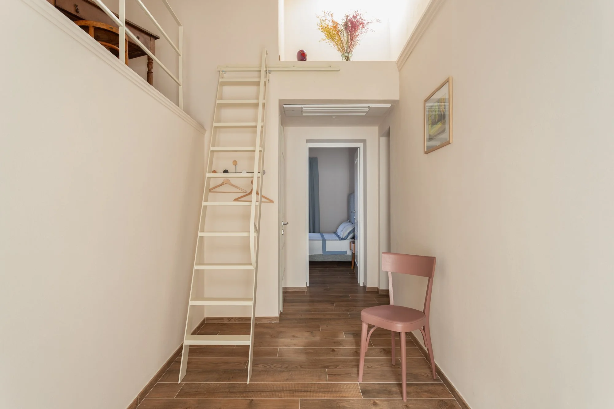 Ingresso con sedia rosa, scala e vista sulla camera da letto