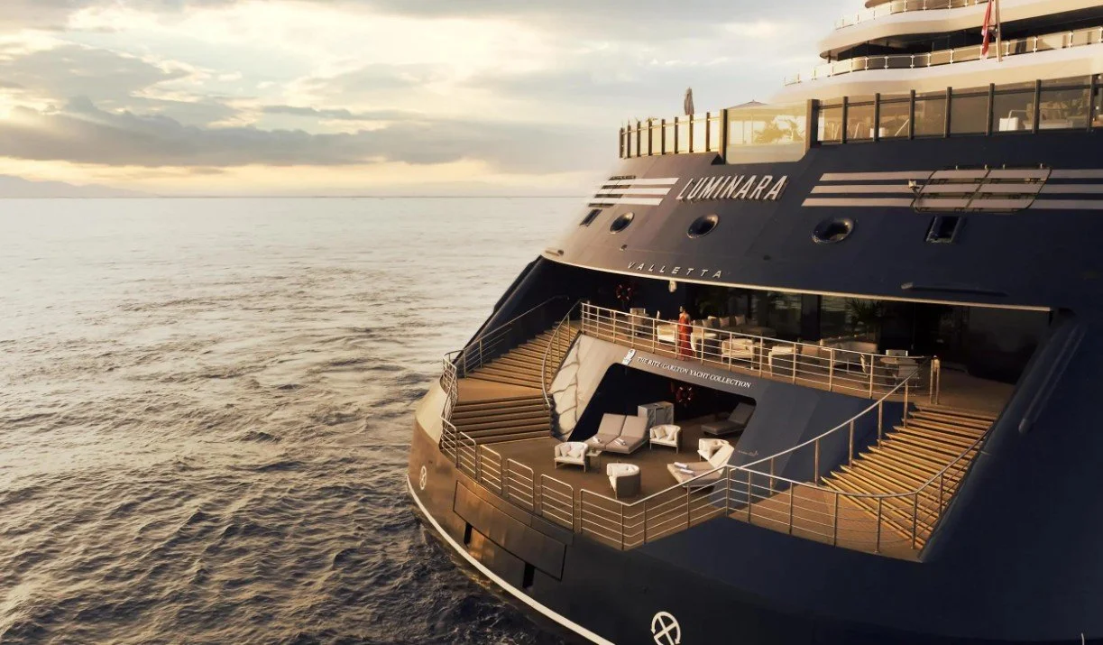 A luxury yacht named LUMINARA on the water during sunset with an outdoor lounge area on the back deck.