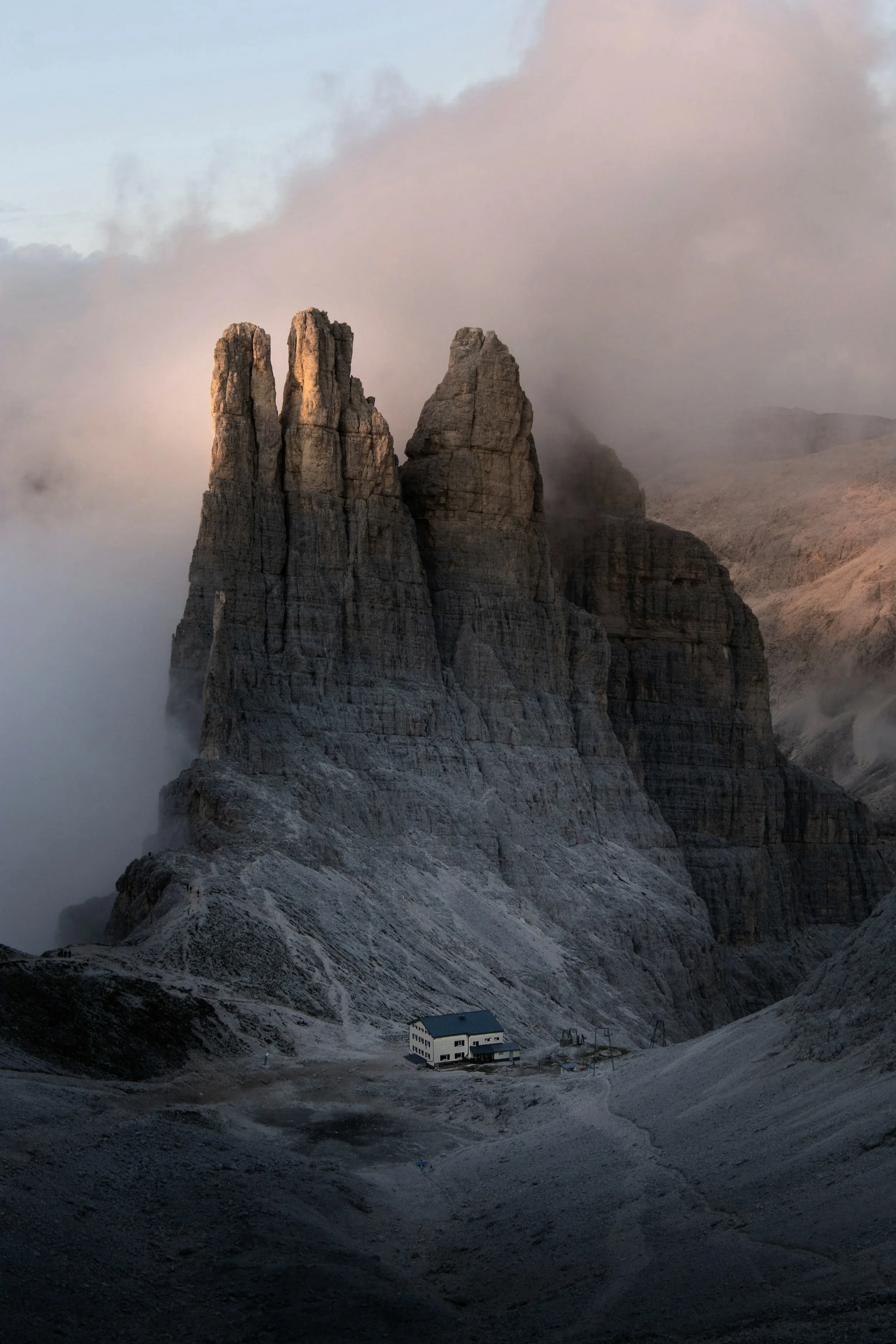 A mountain scene with tall, rugged rock formations partially obscured by mist and clouds. There is a small building at the base of the mountains.