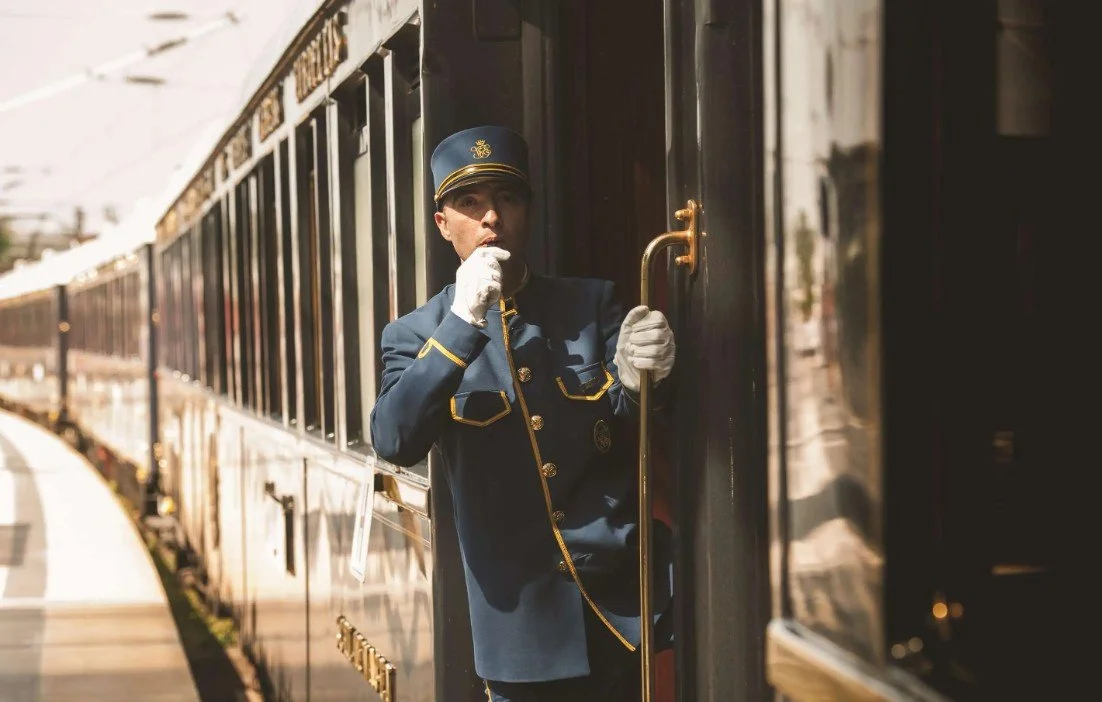 Train station conductor in uniform standing at the train door, holding the door handle, and blowing a whistle.