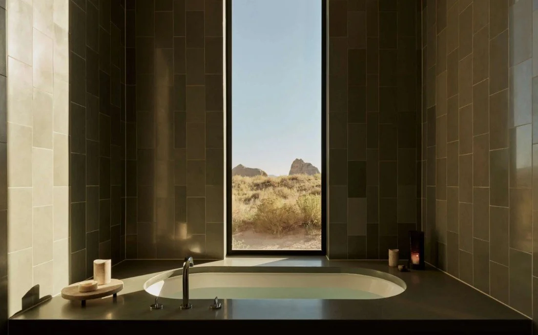 Modern bathroom with a built-in bathtub, candles, and a large window showing a desert landscape with mountains.