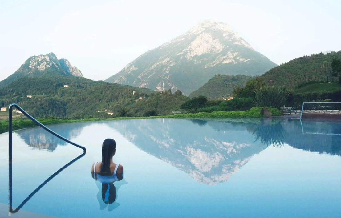 A woman relaxing in an infinity pool with mountain scenery reflected in the water.