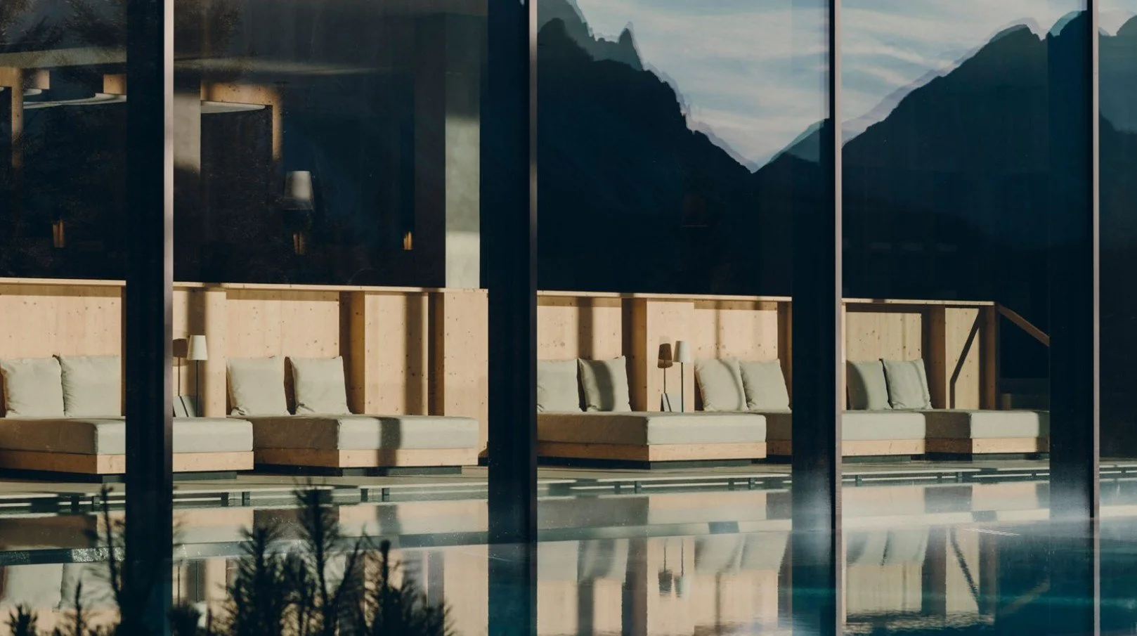 Indoor sitting area with beige couches and matching pillows, large window with mountain landscape view, reflections on the glass, modern decor.