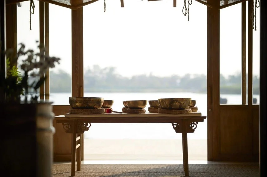 A wooden table with stacked bowls inside a gazebo overlooking a body of water with trees in the distance.