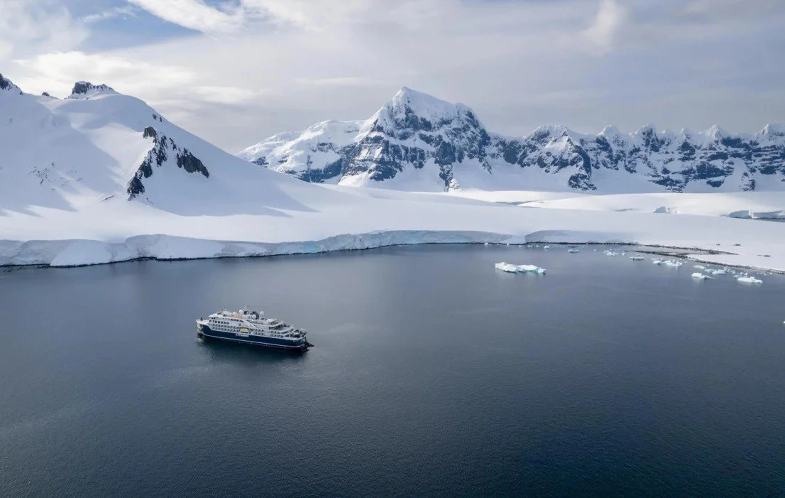 A cruise ship anchored in icy waters surrounded by snow-covered mountains and glaciers.