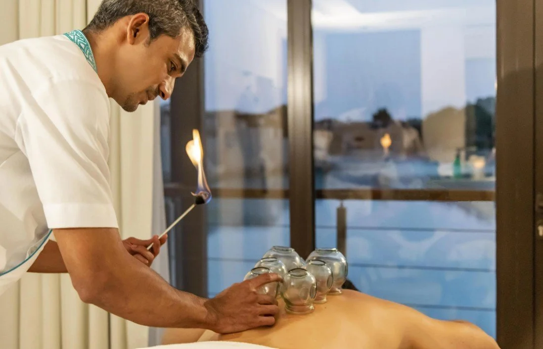 A chef lighting shot glasses on a person's back with a matchstick.