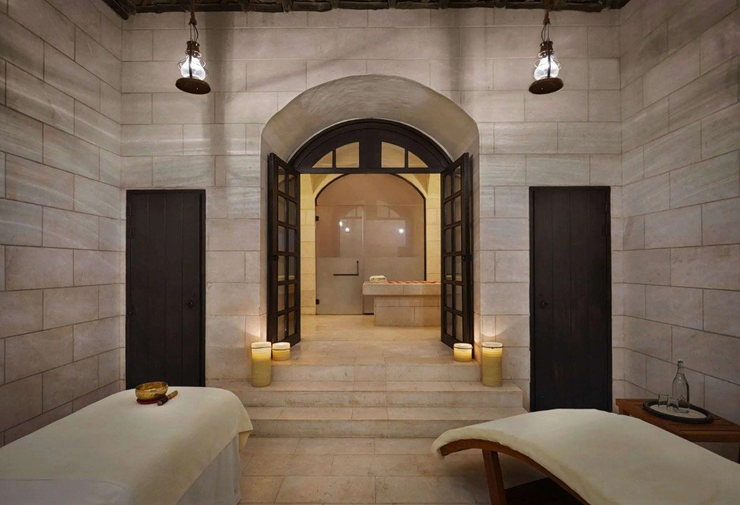 Interior of a spa or massage room with two massage tables and candles, viewed through large open doors.