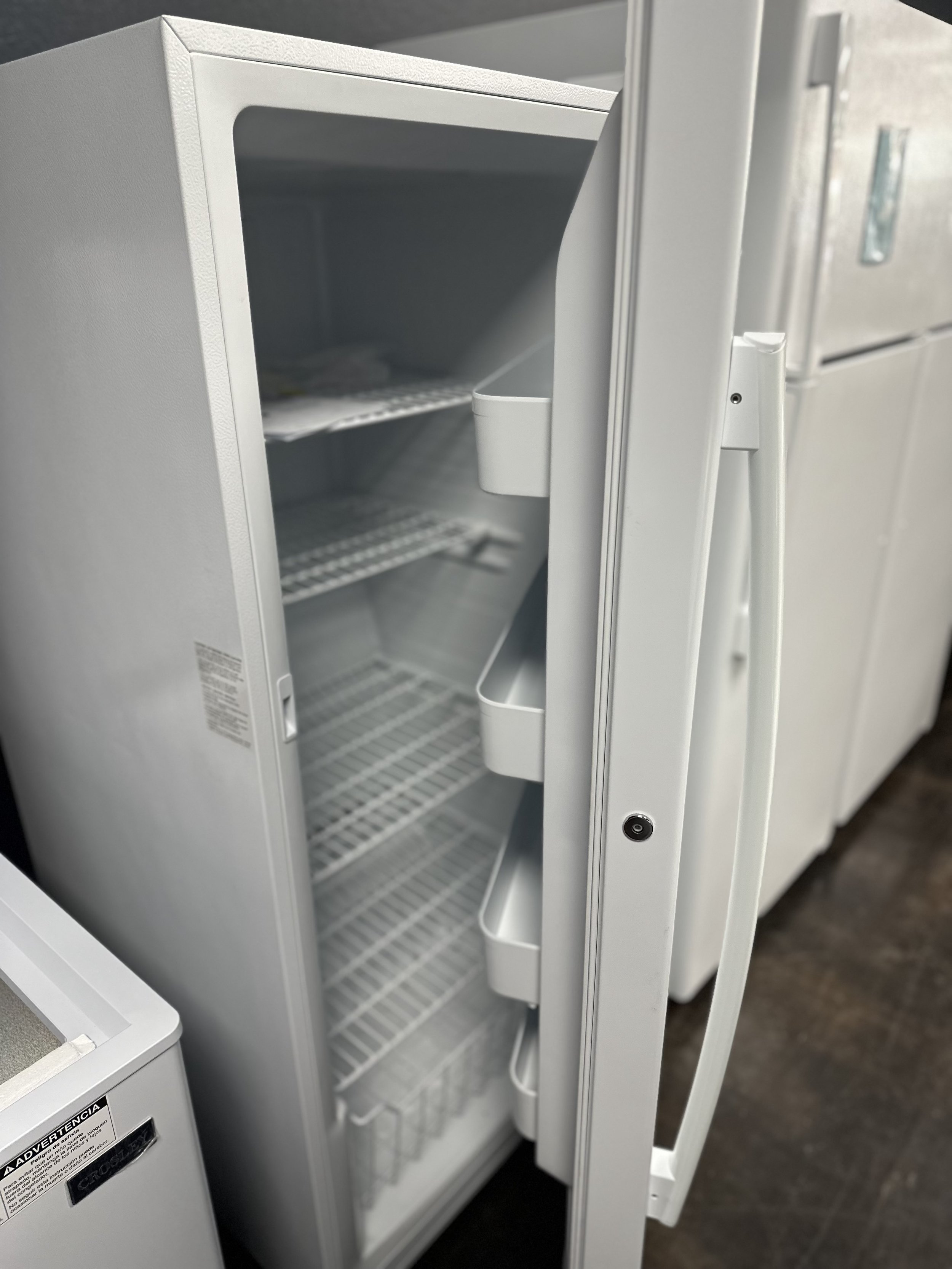 Empty white mini fridge with open door showing wire shelves and door compartments in a laundry room or kitchen.
