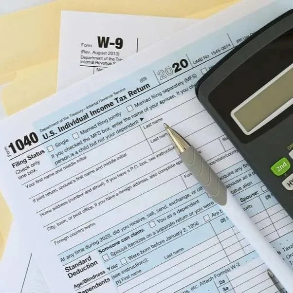 U.S. Individual Income Tax Return (Form W-9) and Form 1040 from 2020 with a silver pen and a calculator on top.