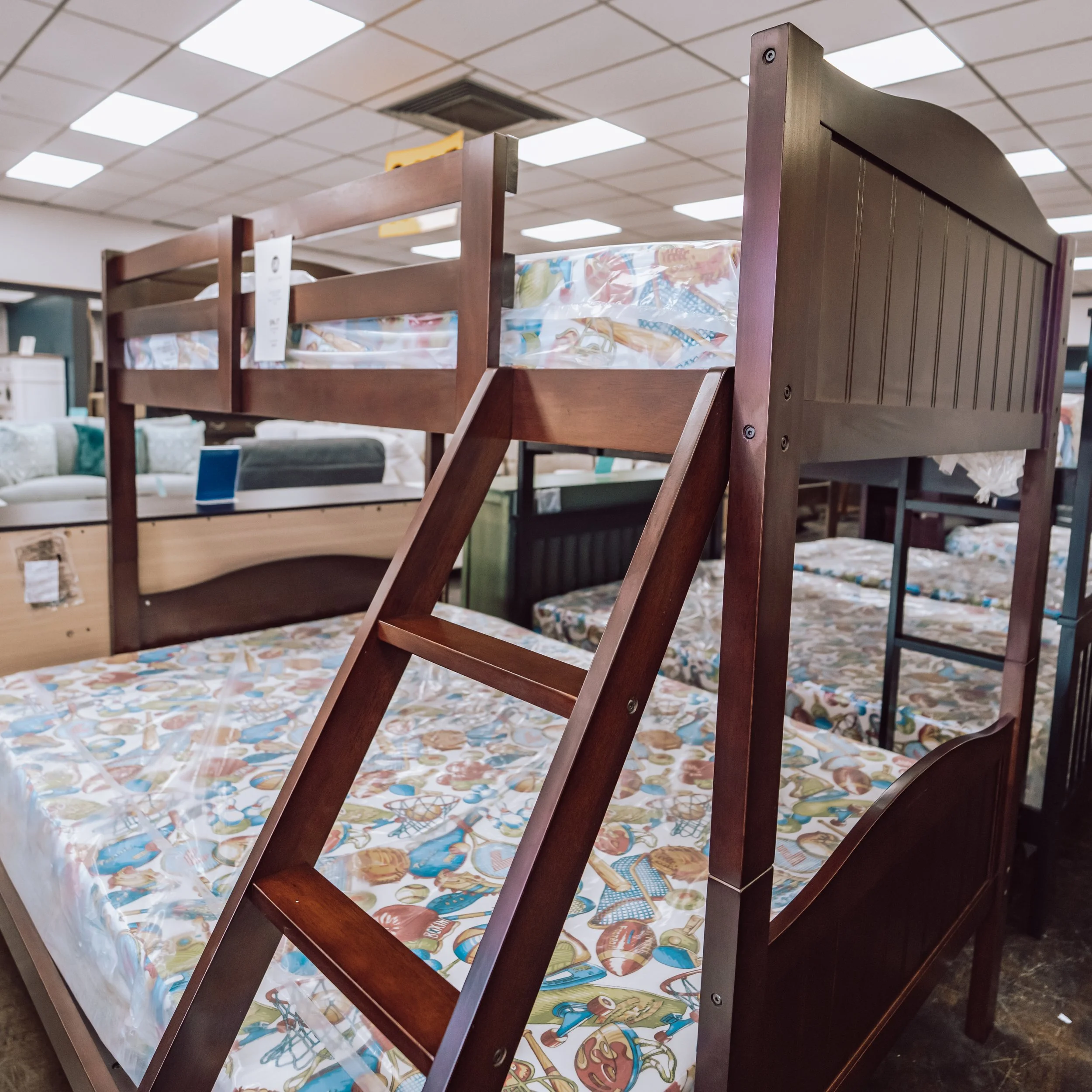 Wooden bunk bed in furniture store, with mattress on top and print sheet on bottom bed.