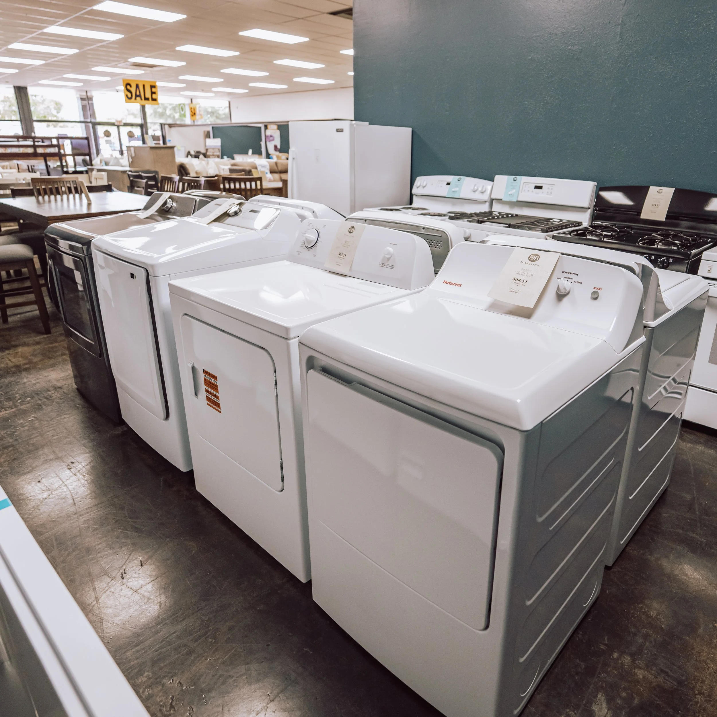 A row of washing machines and dryers displayed for sale in a store with signs indicating a sale.