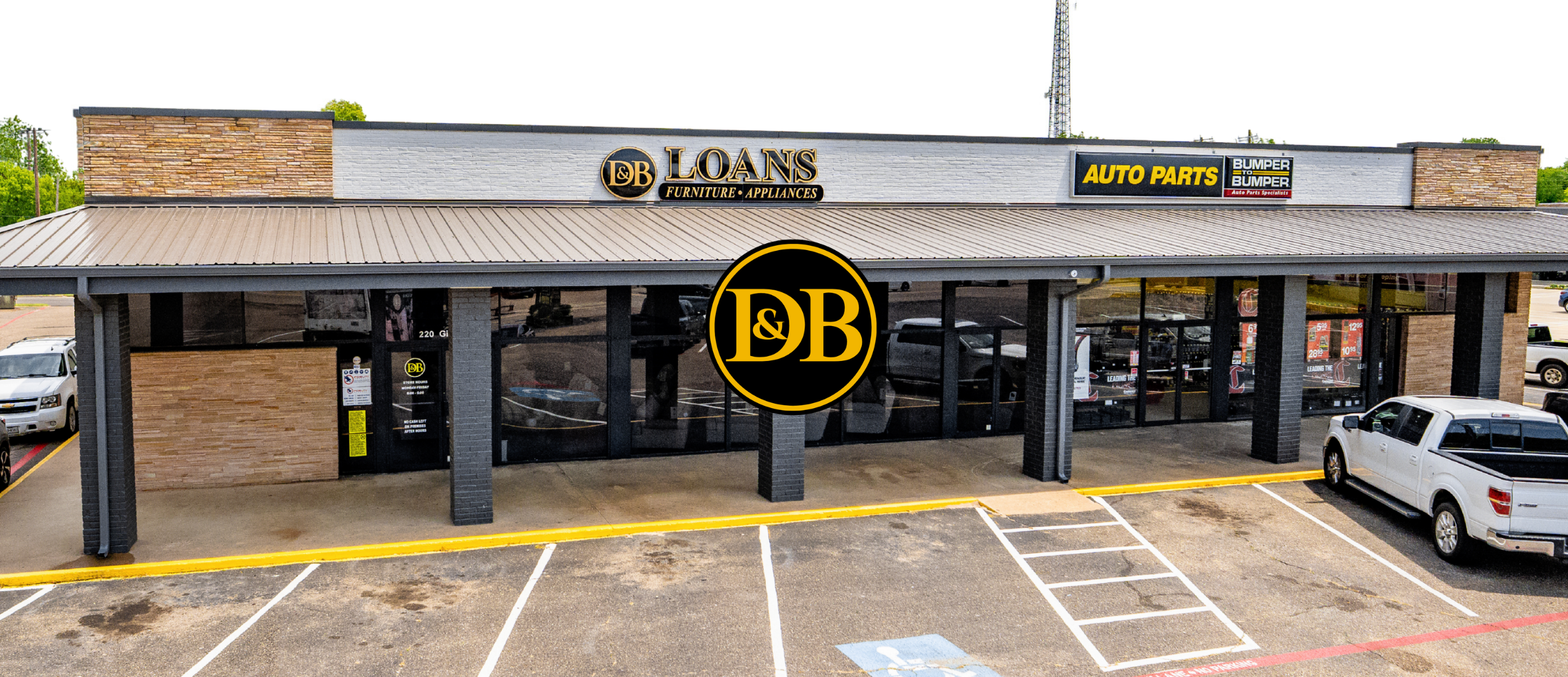 Exterior view of a retail store named D&B Loans Furniture Appliances with signage indicating auto parts, located in a strip mall with a parking lot in front, and a few cars parked along the sides.