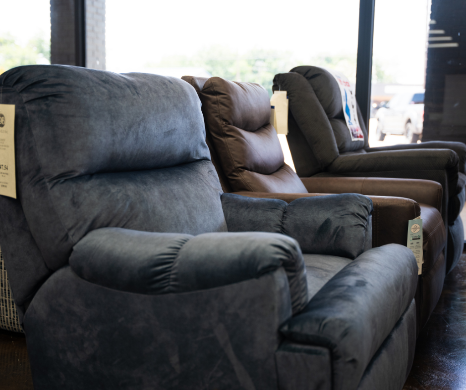 Two recliner chairs, one beige and one dark gray, displayed in a furniture store with signs on top indicating they are lift chairs.