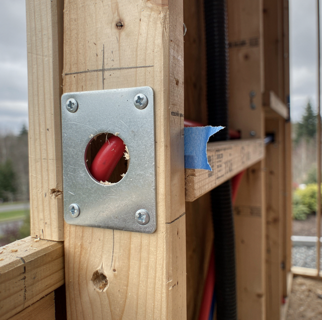 A red button mounted in a metal plate on a wooden post with blue tape nearby.