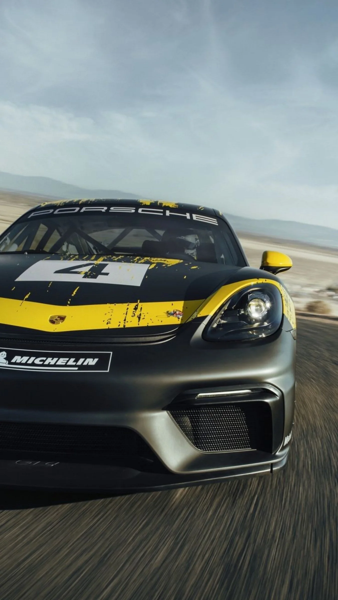 Black and yellow Porsche Cayman GT4 driving on a race track in the desert.