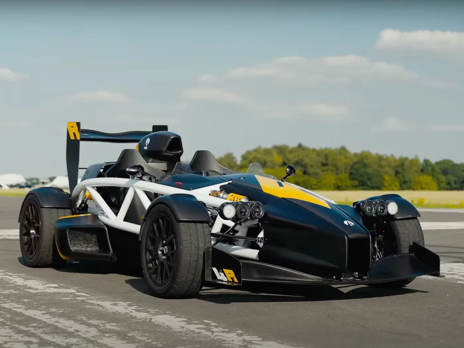 Black and yellow race car on a runway with a blue sky and green trees in the background.