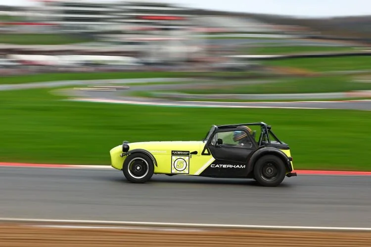 A black and yellow Caterham sports car racing on a track with a blurred background indicating high speed.
