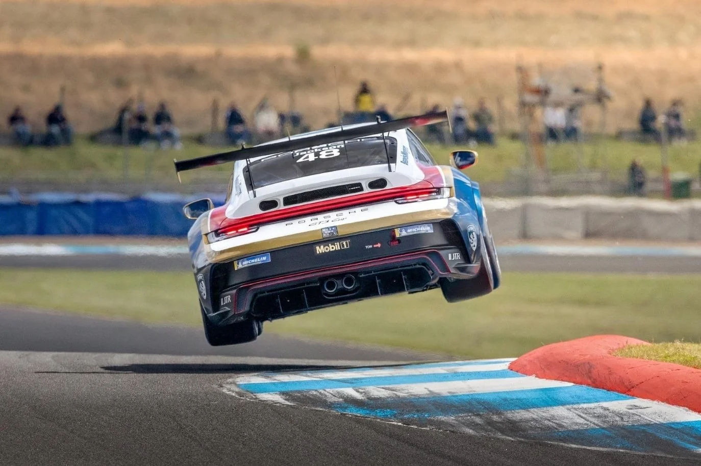 A race car jumps off a curb at Knockhill race track, Dunfermline, Scotland. Spectators in the background.