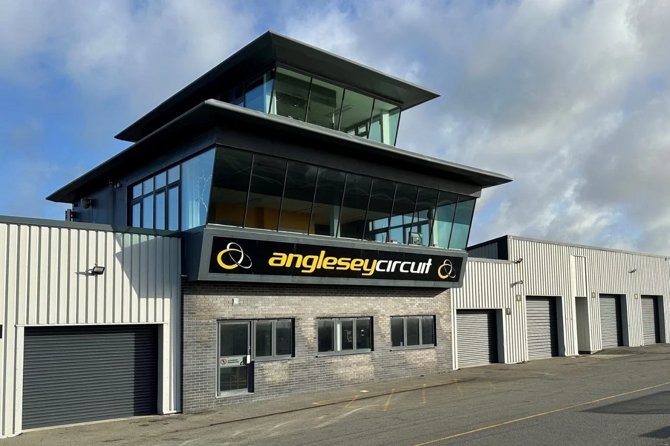 Exterior view of the Anglesey Circuit building with a modern glass and metal design, including a sign that reads 'anglesey circuit' on the front.