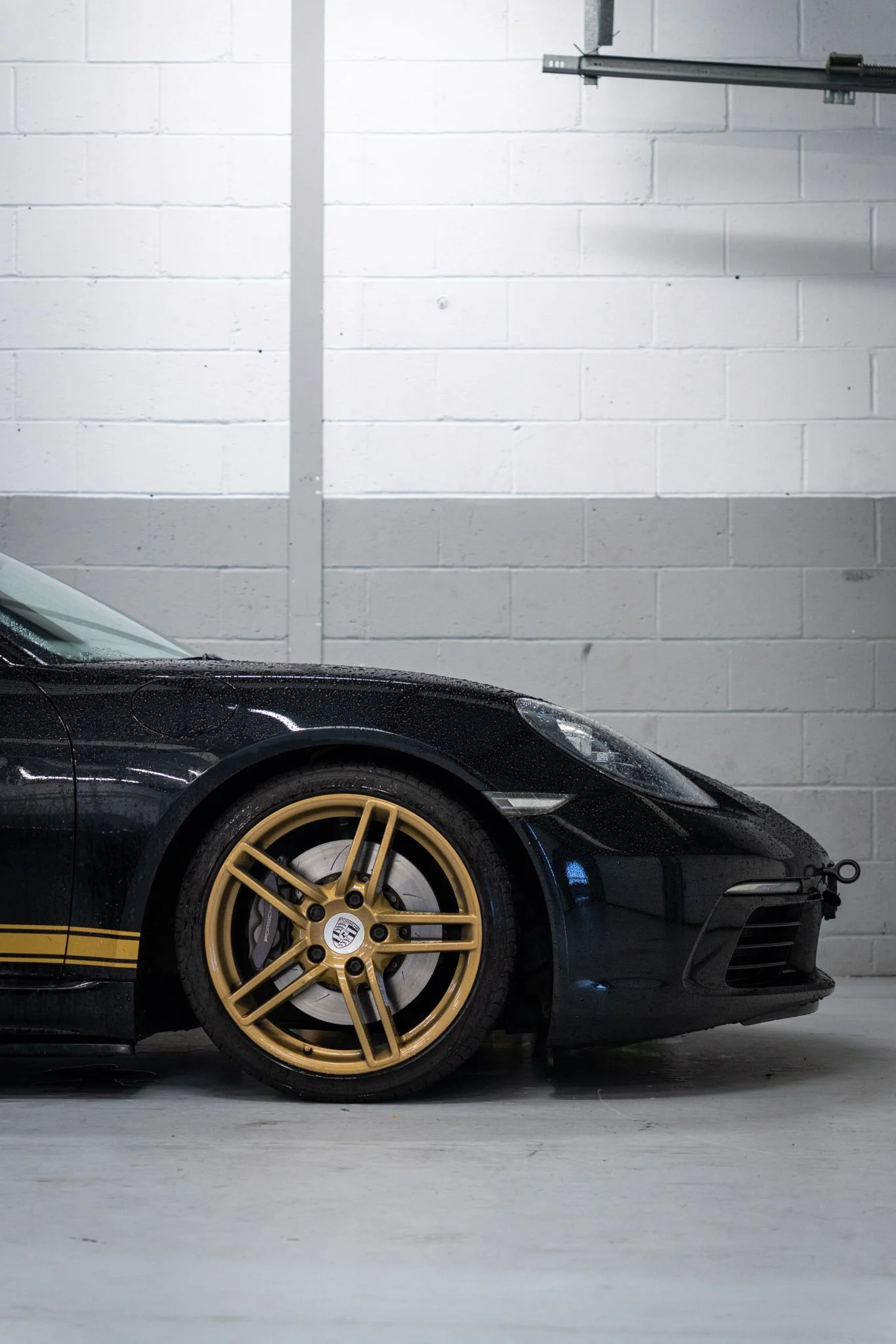 A black and gold Porsche Cayman in a pit lane garage at Silverstone during a private corporate event.