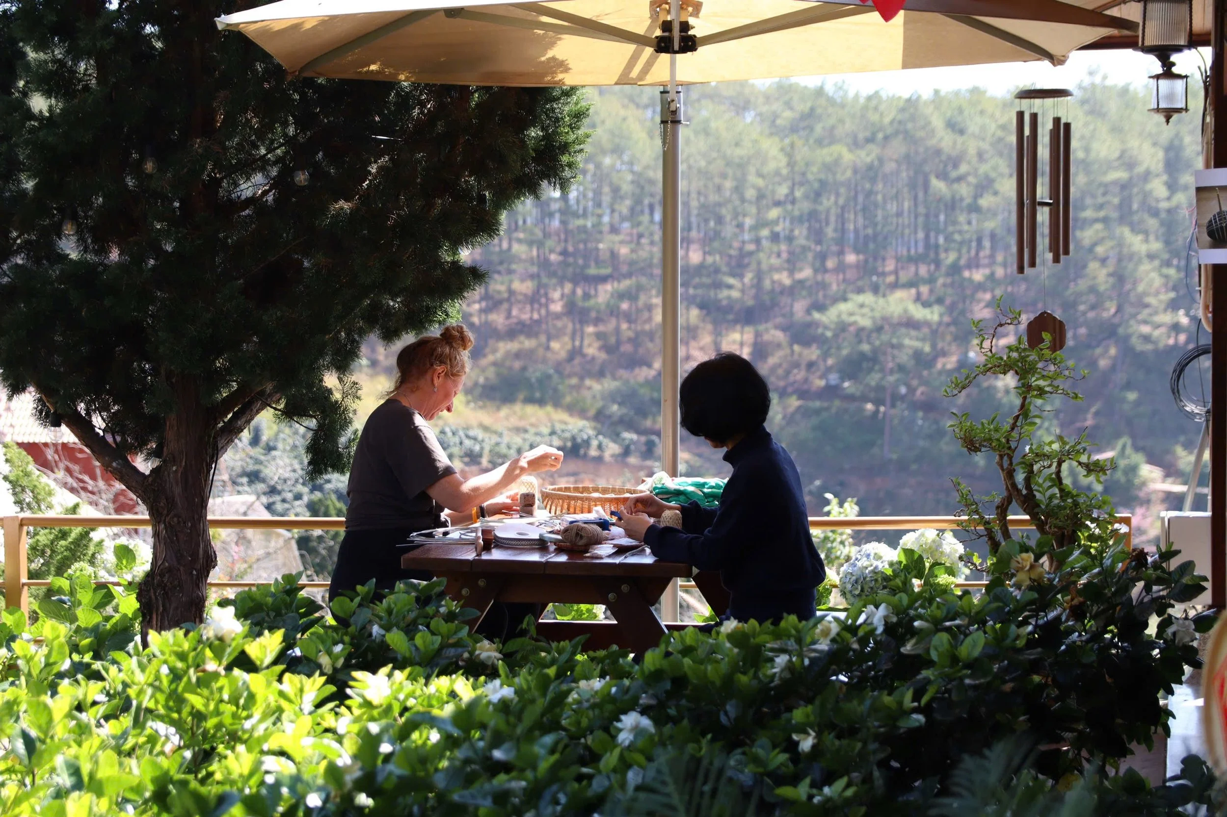 A group of people sitting on a wooden pavilion in a forest, engaging in conversation or activity. A dog is lying on the ground nearby.