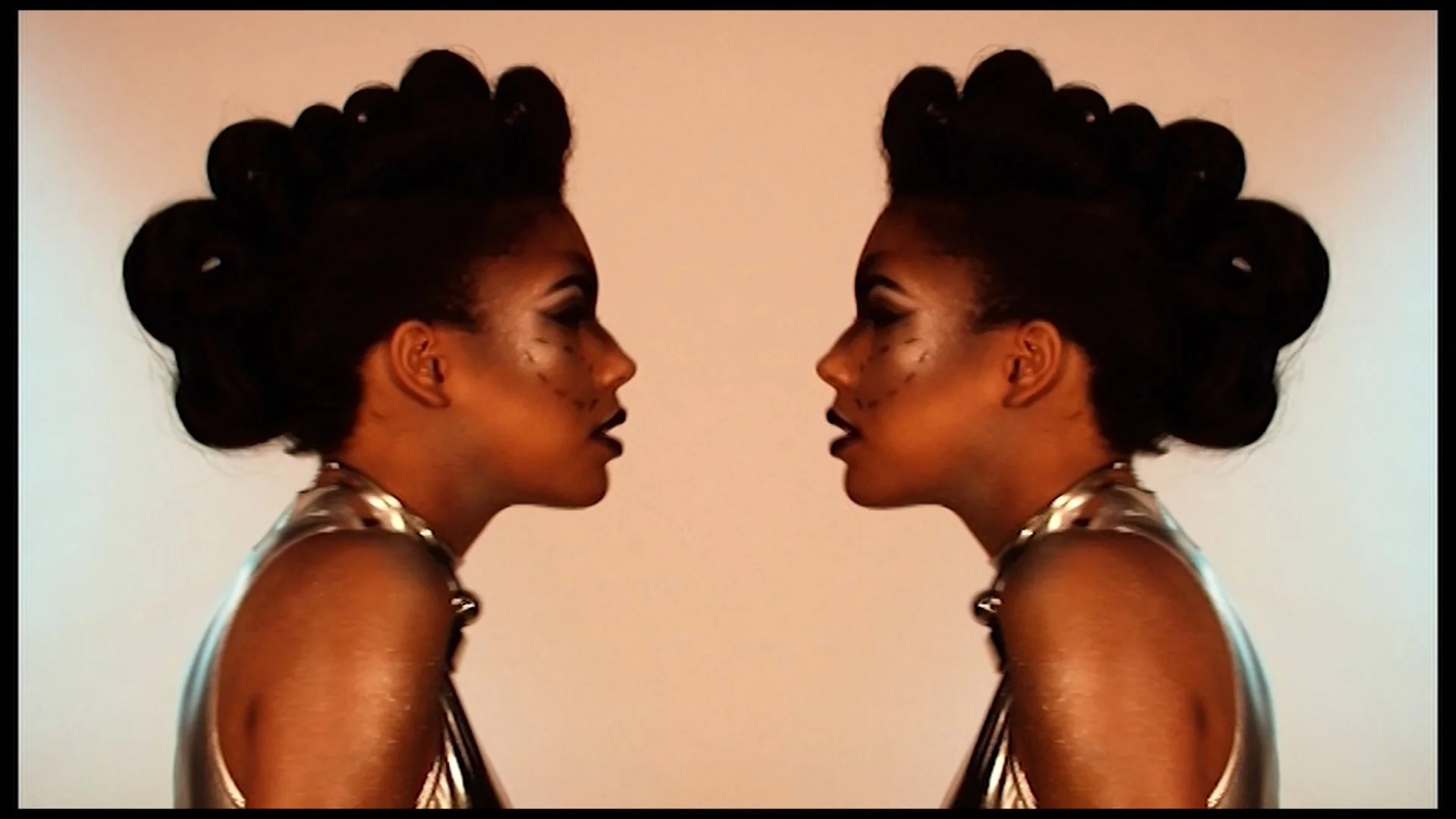 Photo of a woman with elaborate curled hair and makeup, looking at her reflection, with mirrored image creating a symmetrical effect.