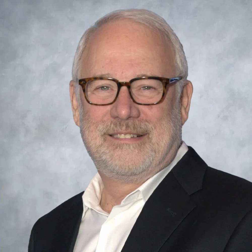 A headshot of man infront of a neutral backdrop
