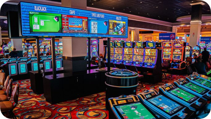 Inside a casino with rows of slot machines, digital screens displaying game information, and colorful patterned carpet.
