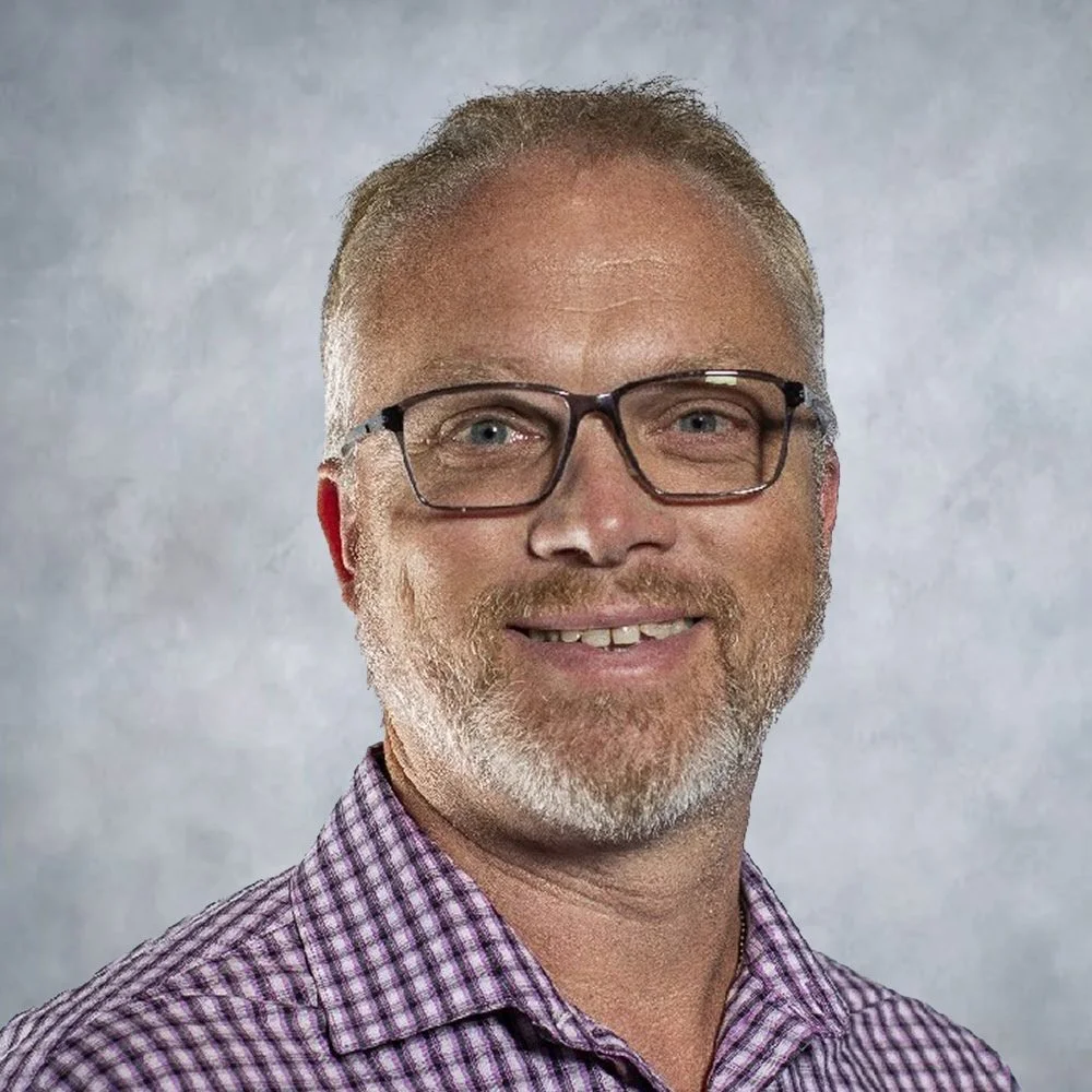 A headshot of man in front of a neutral backdrop