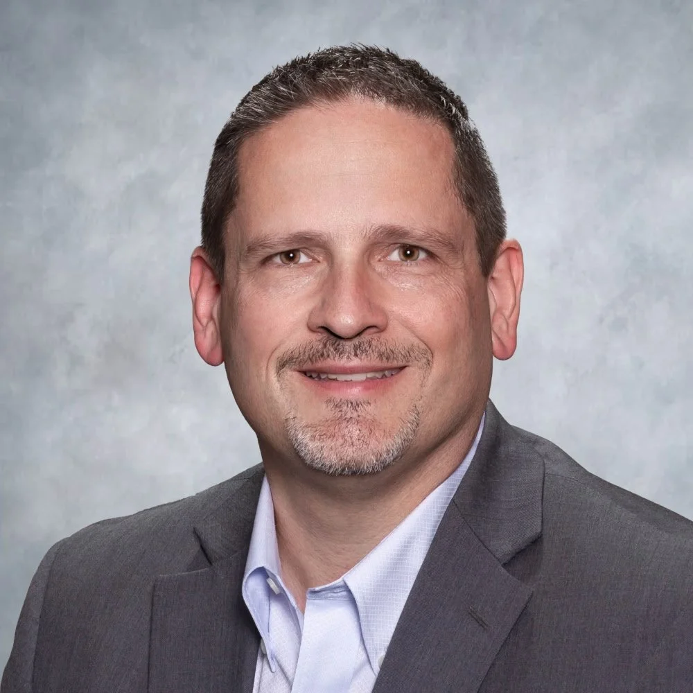 A headshot of man in front of a neutral backdrop