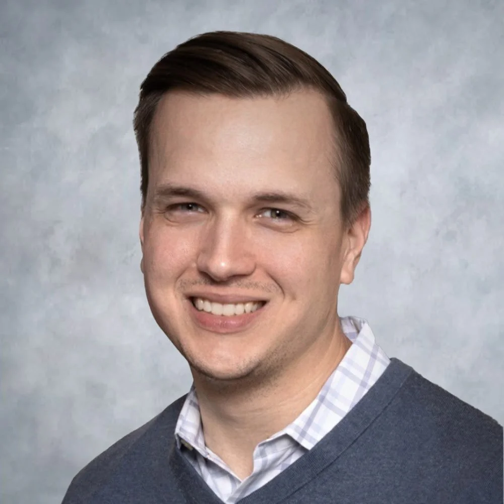 A headshot of man in front of a neutral backdrop